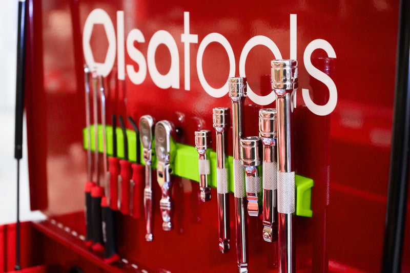 Assortment of tools being held by a green Olsa Tools silicone magnetic tool holder inside of a toolbox.