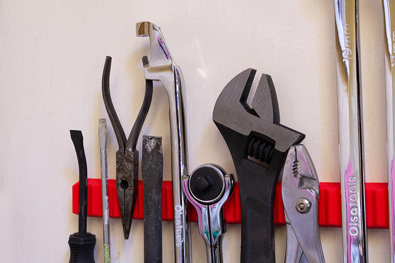 The Olsa Tools red silicone magnetic tool holder mounted on the wall with a lot of tools hanging from it.